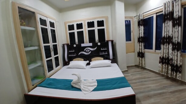 A neatly made bed with a blue and white bedspread, a decorative swan pillow, and a headboard with an eye design. - Rudraksh Home Stay (Varanasi)