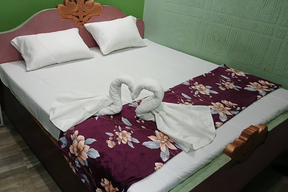 Una cama bien hecha con una colcha floral y una toalla blanca dispuesta en forma de corazón.
