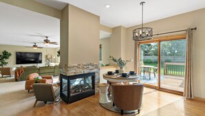 A spacious living room with a fireplace, a ceiling fan, a TV, and a dining area with a view to the outdoors. - 1/2 Acre Retreat: 100" TV, Open layout Navy Base and Six Flags Great America (Gurnee)