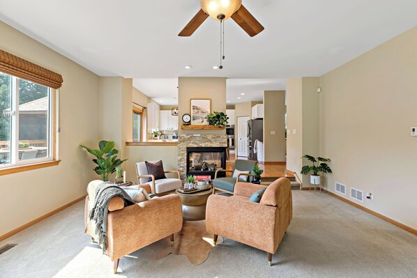 A spacious living room with a fireplace, comfortable seating, and a ceiling fan.