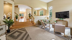 A spacious living room with a large TV, comfortable seating, and a staircase leading to another area. - 1/2 Acre Retreat: 100" TV, Open layout Navy Base and Six Flags Great America (Gurnee)
