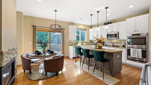 A modern kitchen with white cabinets, stainless steel appliances, and a central island with bar stools. - 1/2 Acre Retreat: 100" TV, Open layout Navy Base and Six Flags Great America (Gurnee)