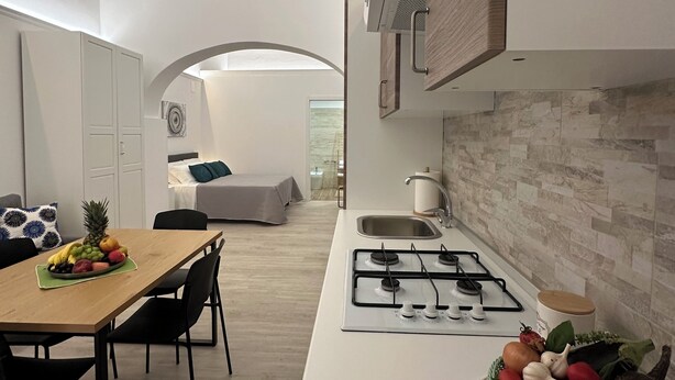 Eine moderne Küche mit weißer Arbeitsplatte, einem Gasherd und einer Essecke mit Tisch für zwei Personen.