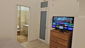 Ein Schlafzimmer mit einem Holzkasten, einem Fernseher, der verschiedene Anwendungen zeigt, einem Badezimmer mit Spiegel und einem Holzboden.