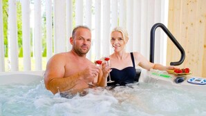 A couple in a hot tub with a wooden interior and a control panel.