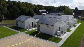 A row of small, modern cabins with metal roofs, arranged in a neat row on a grassy area with a paved walkway in front.