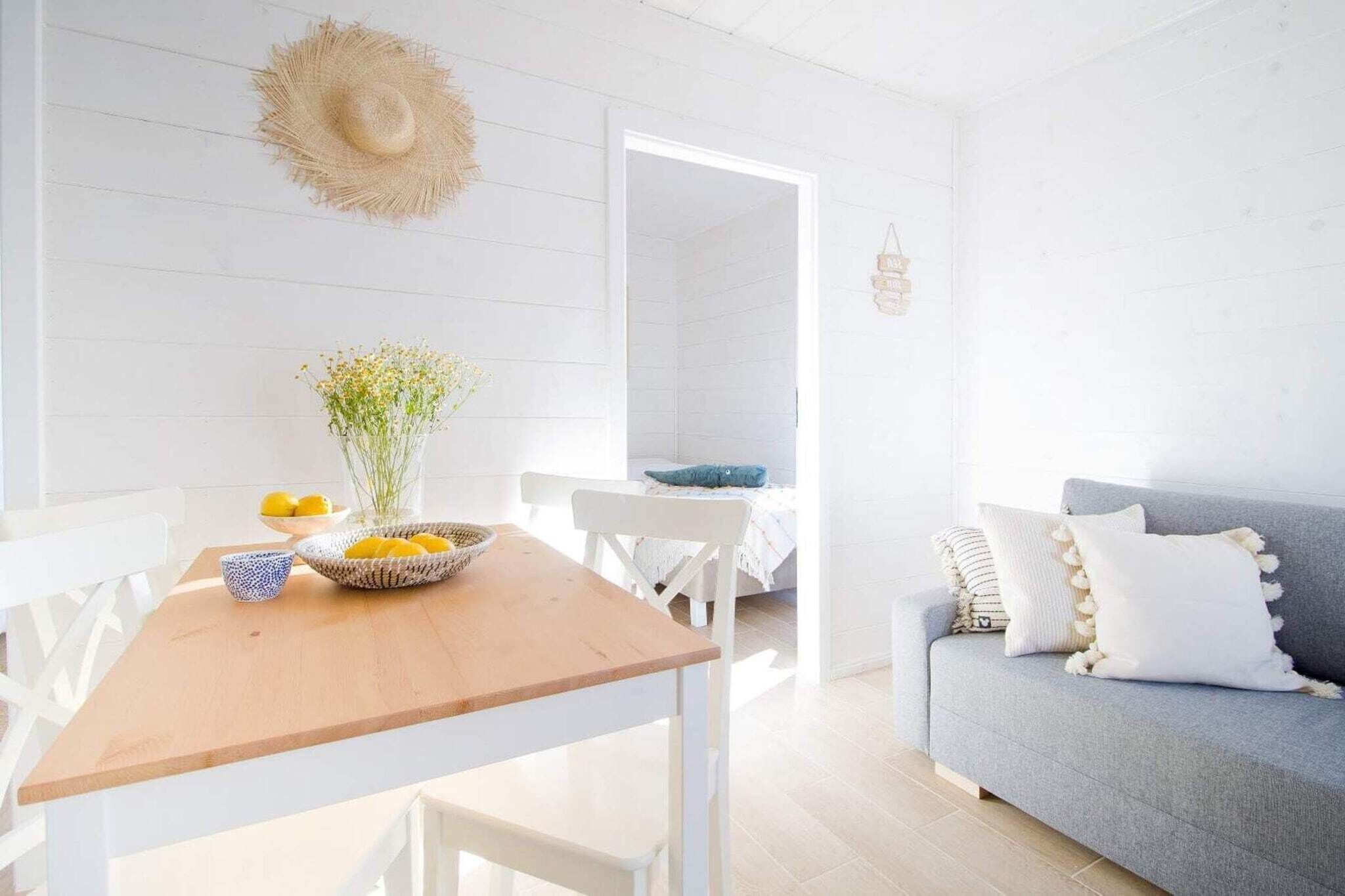 A bright, white-walled room with a wooden table, a grey sofa, and a wicker basket with lemons.