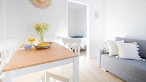 A bright, white-walled room with a wooden table, a grey sofa, and a wicker basket with lemons.
