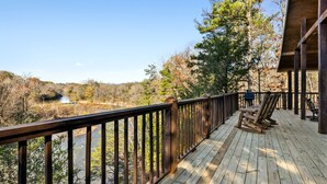A wooden deck with a railing overlooking a river and forested area.