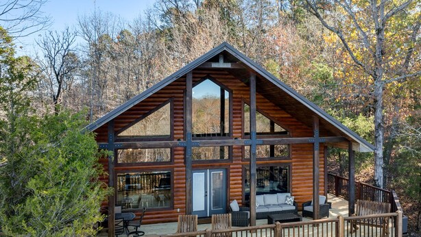 A log cabin with a deck, outdoor seating, and a large window overlooking the forest.