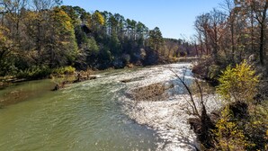A river flowing through a forested area with trees and a cabin in the background.