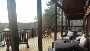 A wooden deck with wicker furniture, a view of a lake, and a covered area with a railing.