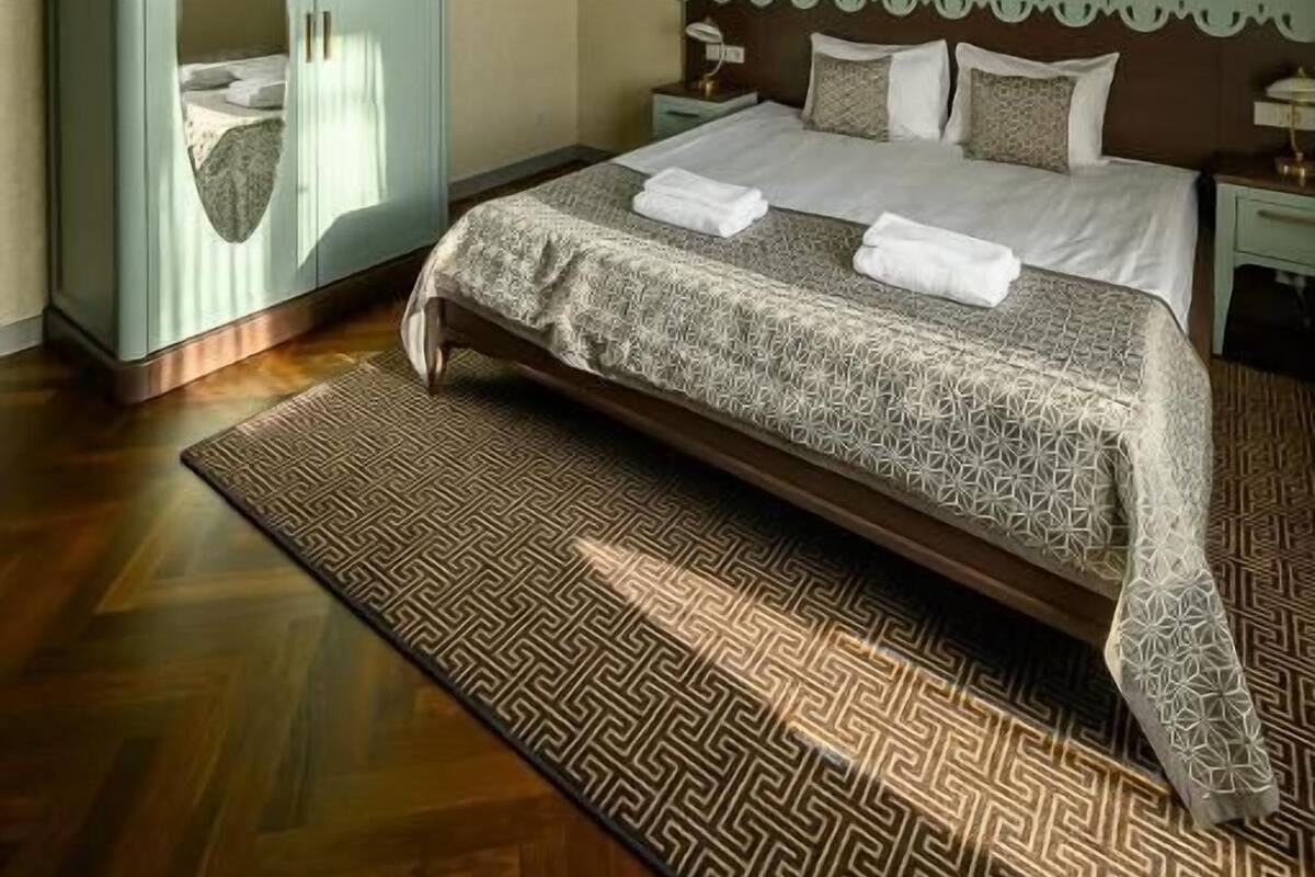 Une chambre avec un grand lit, une armoire, un lustre et un tapis à motifs.