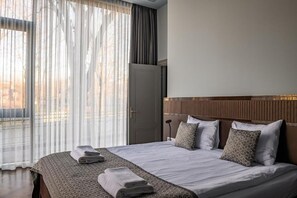 A hotel room with a large bed, a wooden headboard, and a view through sheer curtains. - Roze Peldu Residence (Liepaja)