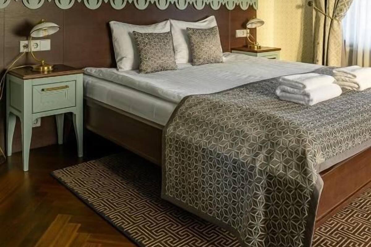 Une chambre à coucher bien rangée, avec un lit, des tables de chevet, un tapis à motifs et un lustre.