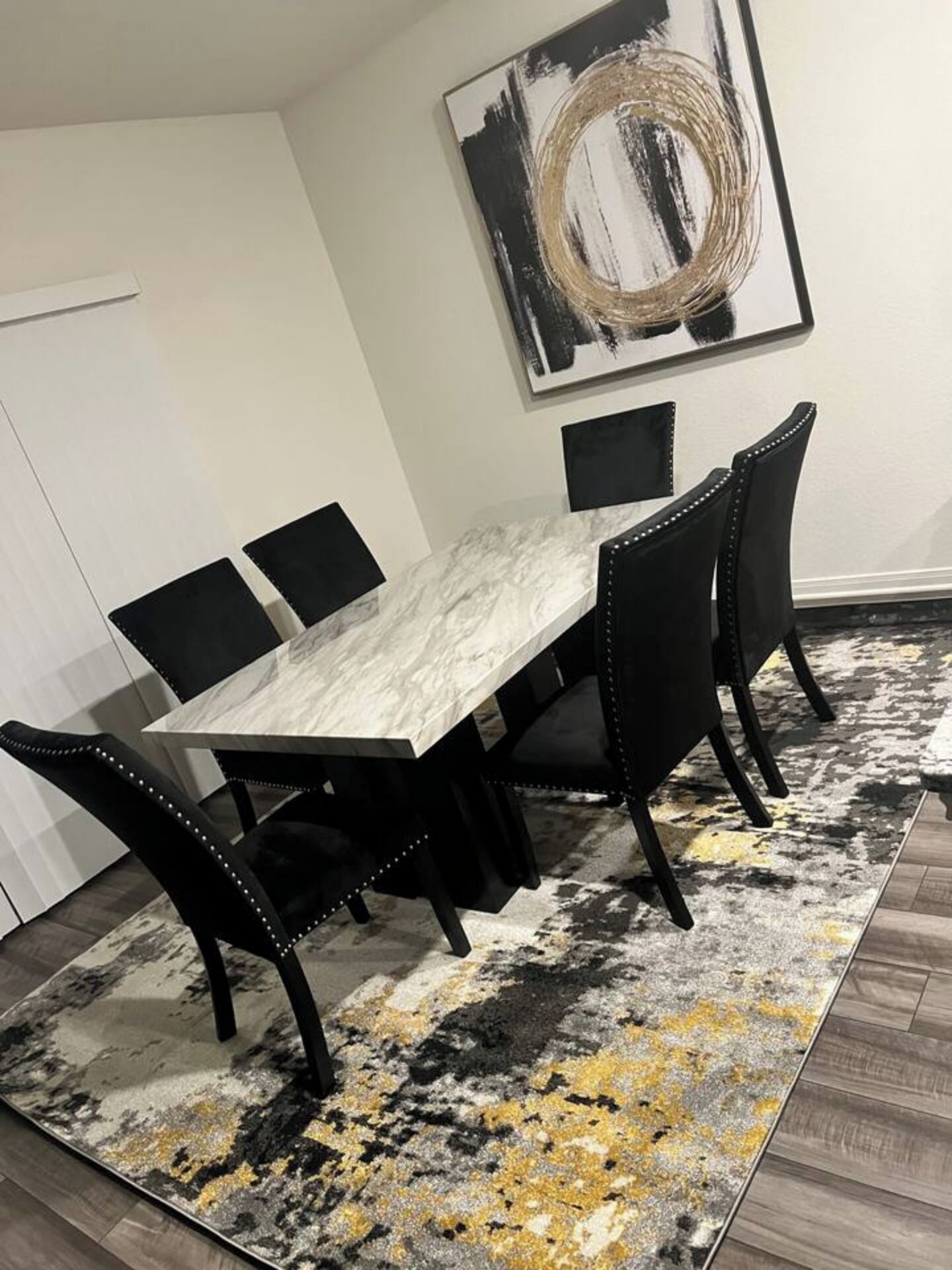 A dining area with a marble table, black chairs, and a black and gold abstract painting on the wall.