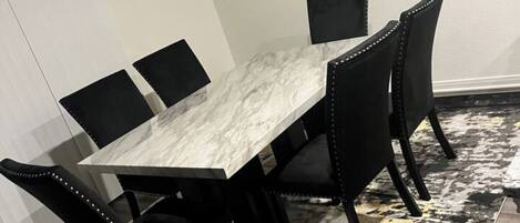 A dining area with a marble table, black chairs, and a black and gold abstract painting on the wall.