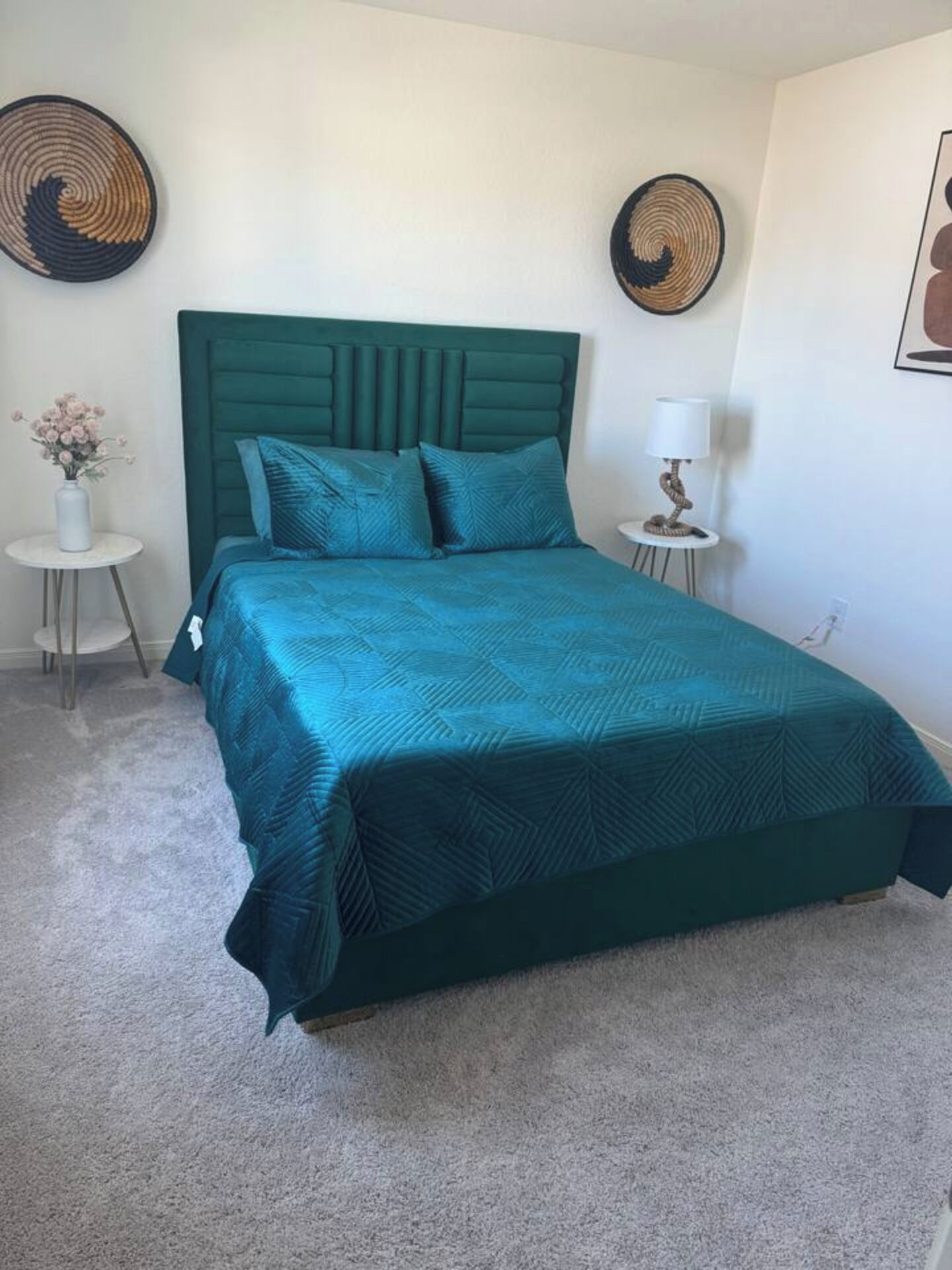 Une chambre à coucher avec une couvre-lit de couleur turquoise, une tête de lit capitonnée et deux petites tables de chevet avec des lampes.