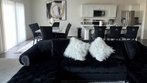 Een moderne woonkamer met een zwarte bank, witte zachte kussens en een kroonluchter.