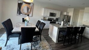 Een moderne keuken met witte kasten, een centraal eiland en een eetgedeelte met een marmeren tafel en zwarte stoelen.