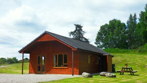 A wooden cabin with a gravel driveway, a picnic table, and a large rock in the foreground.