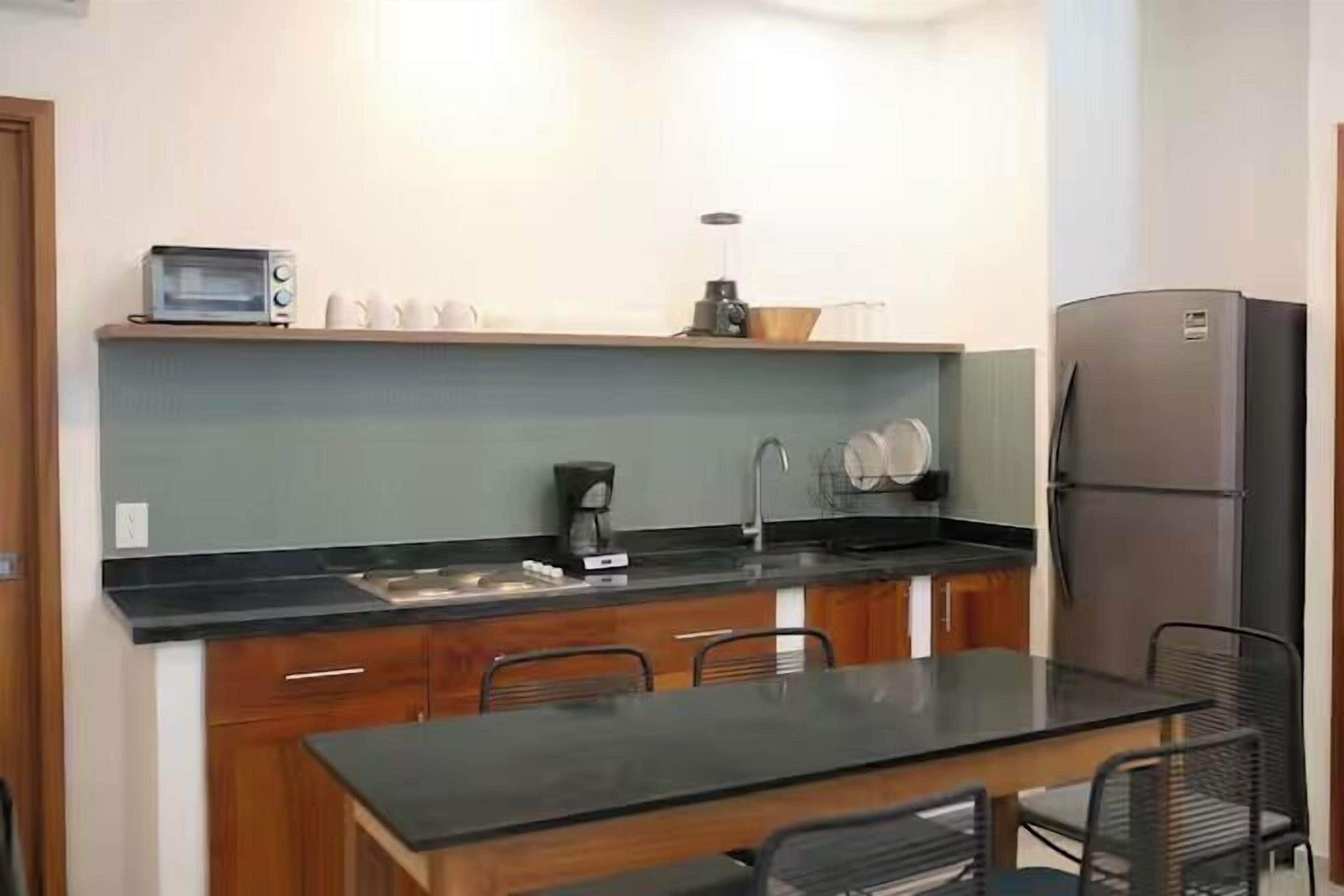 A compact kitchen with a black countertop, a built-in oven, a coffee maker, and a refrigerator.