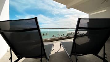 Een balkon met twee zwarte stoelen van netstof, gericht op een helder uitzicht over de oceaan en palmbomen.