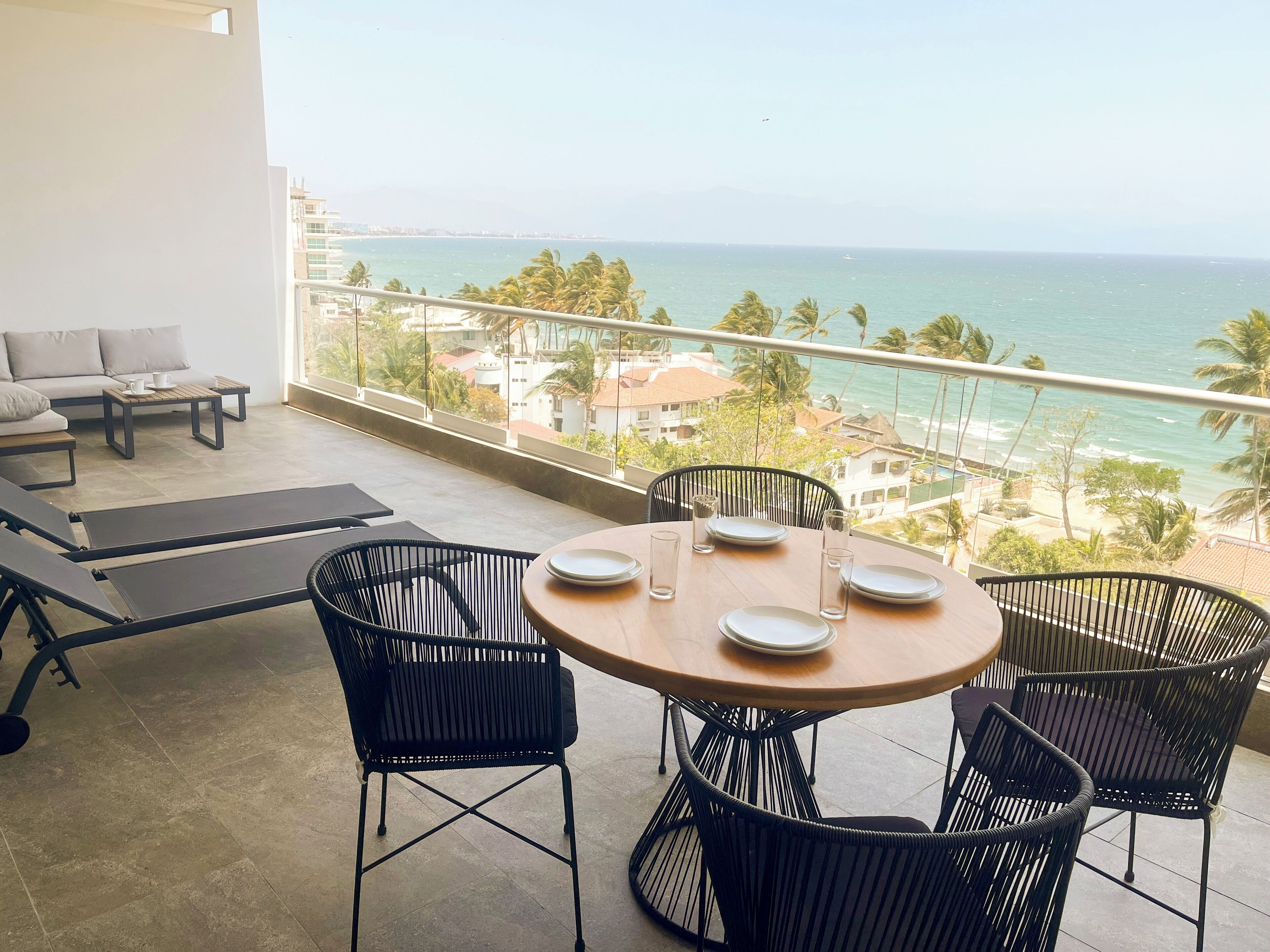 A balcony with a view of the ocean, a round table with chairs, and a sofa.