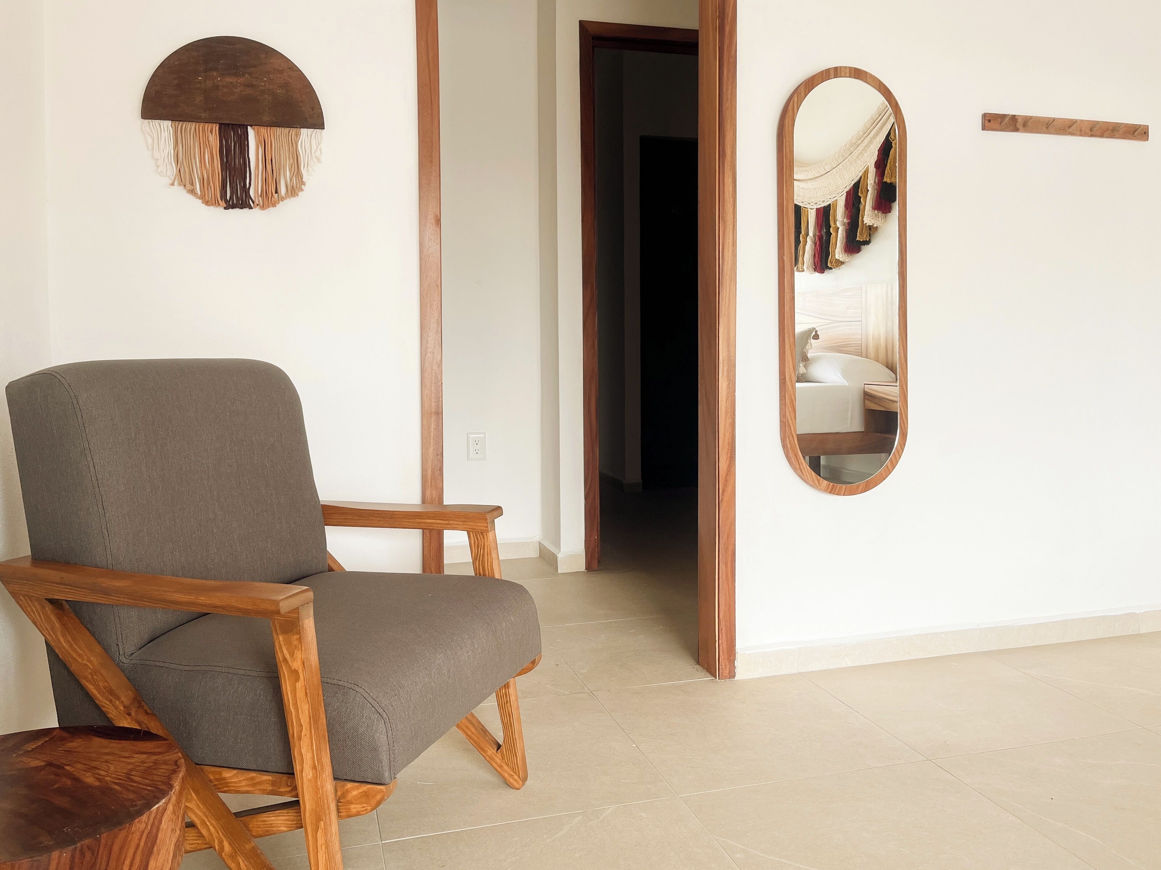 A room with a wooden chair, a round mirror, and a hanging macrame piece.