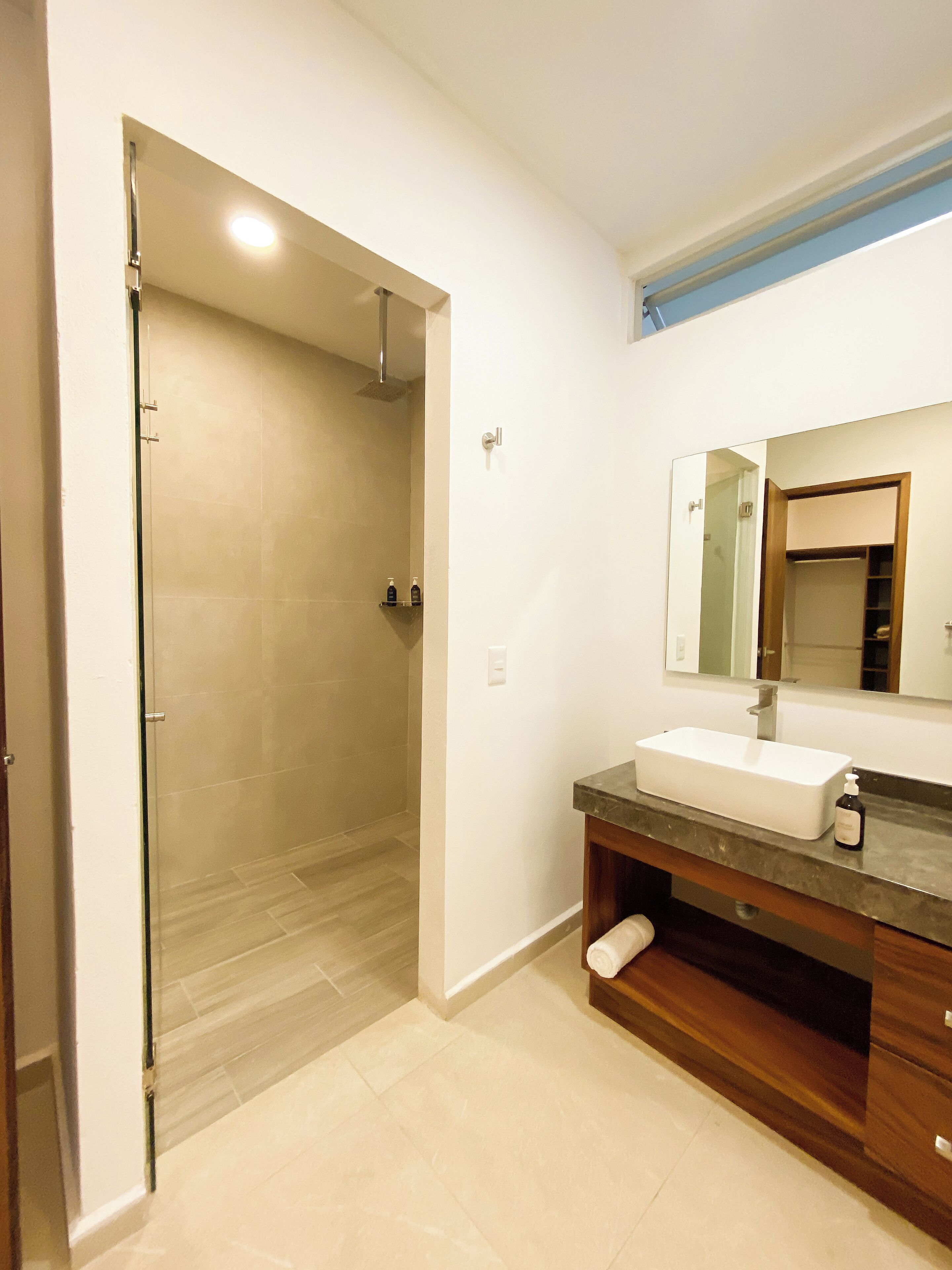 A bathroom with a glass shower door, a white sink, and a wooden vanity.