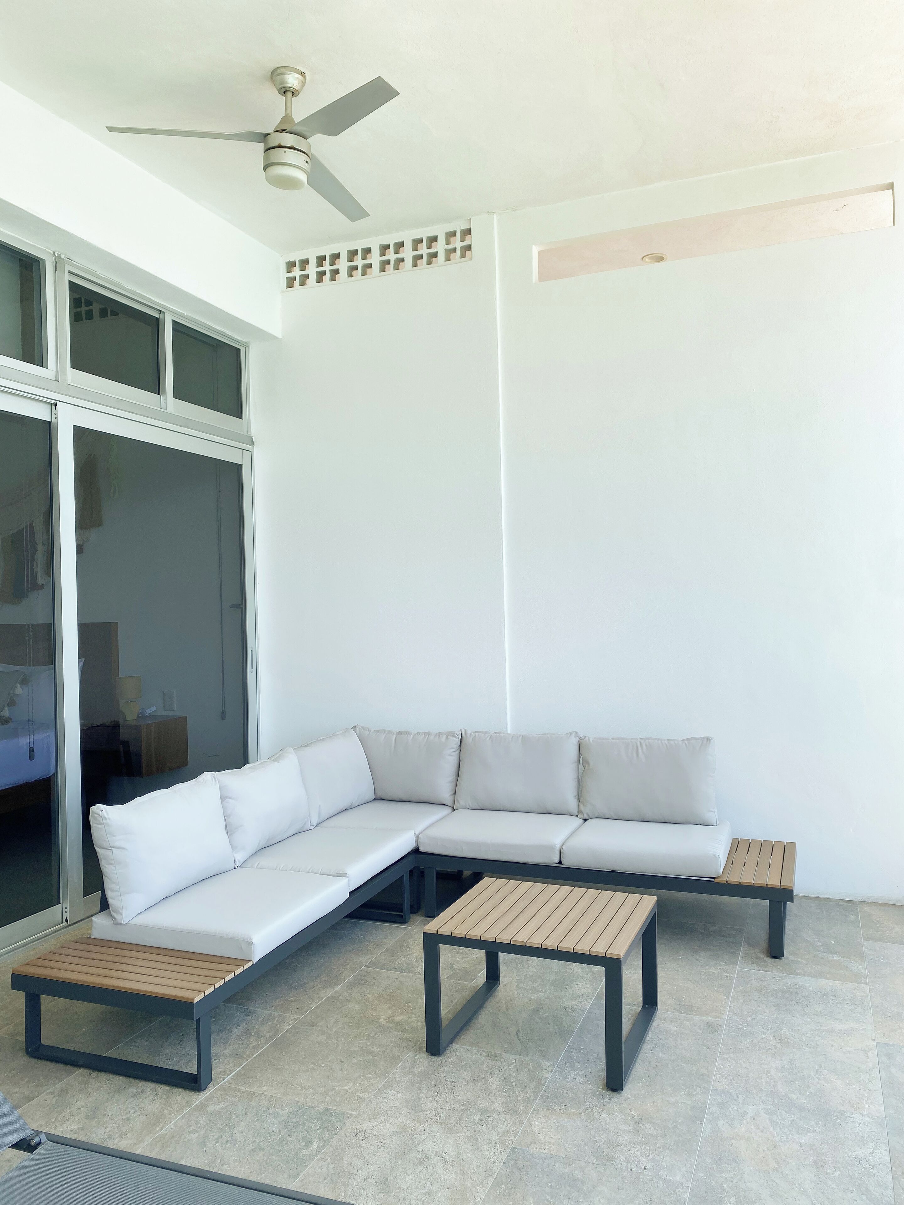 A modern, minimalist room with a sectional sofa, two wooden tables, and a ceiling fan.