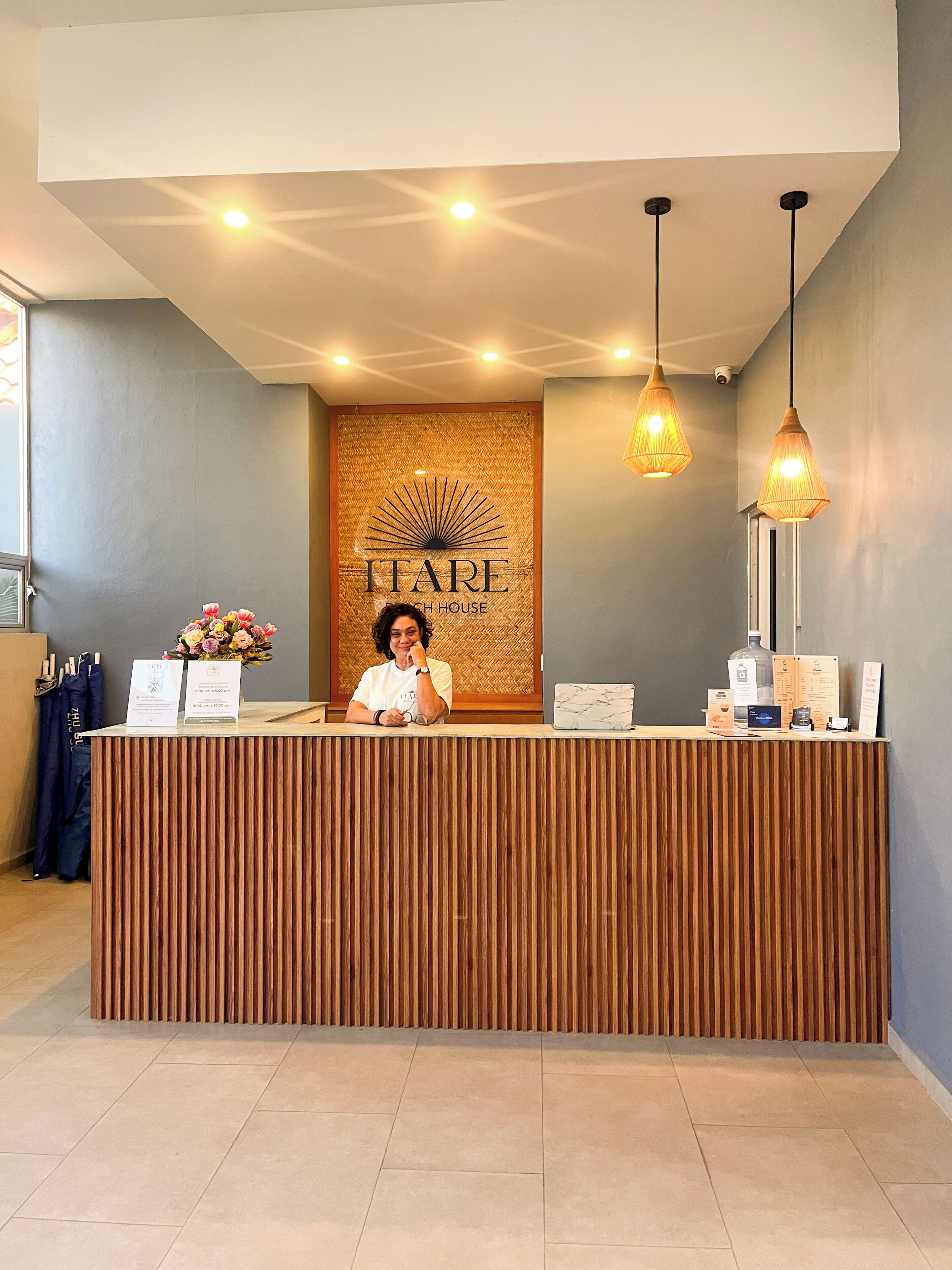 A reception desk with a wooden finish, a wall with a sunburst design, and two hanging pendant lights.