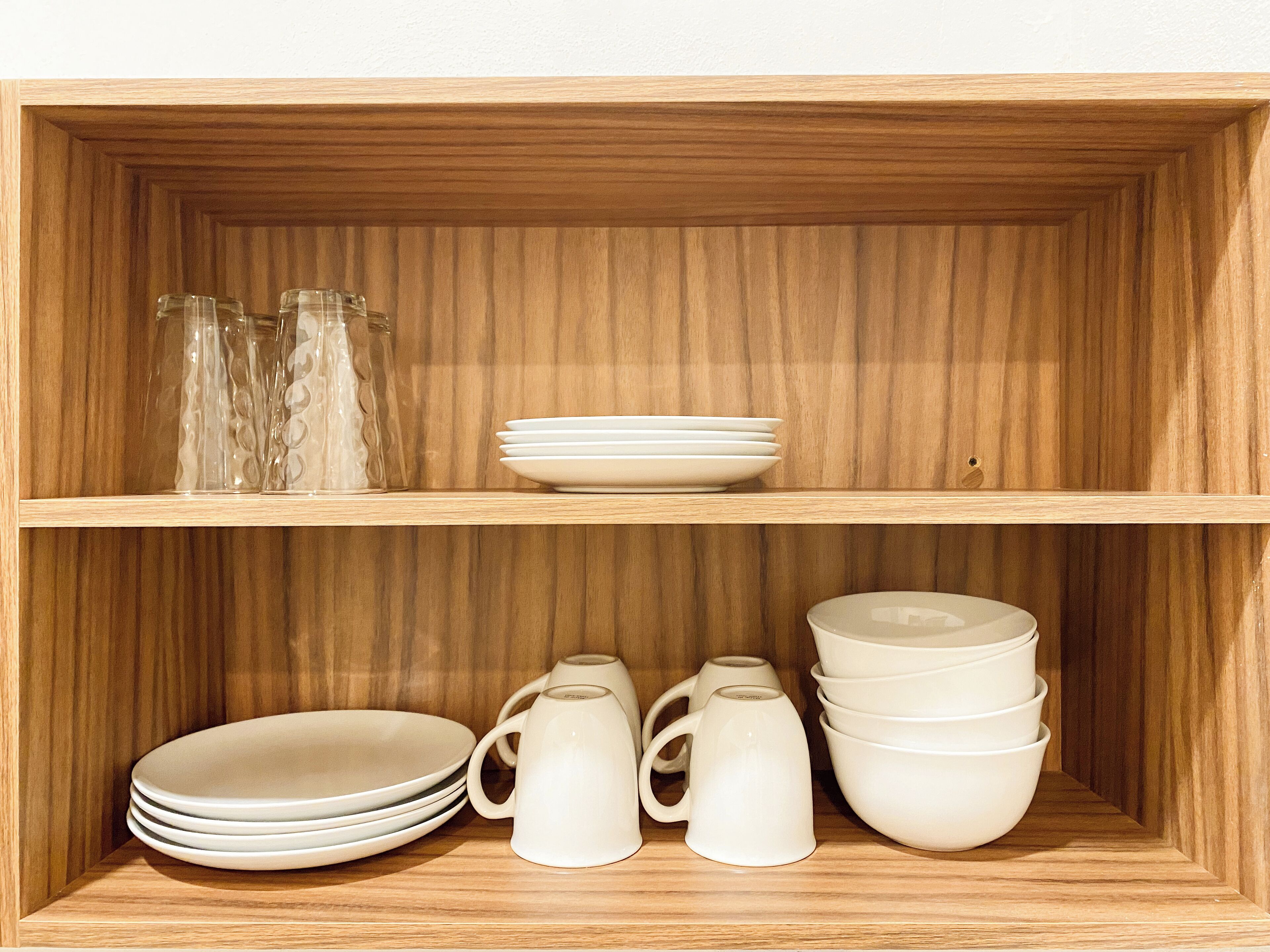 Una estantería de madera con platos, tazones y cristalería blancos.