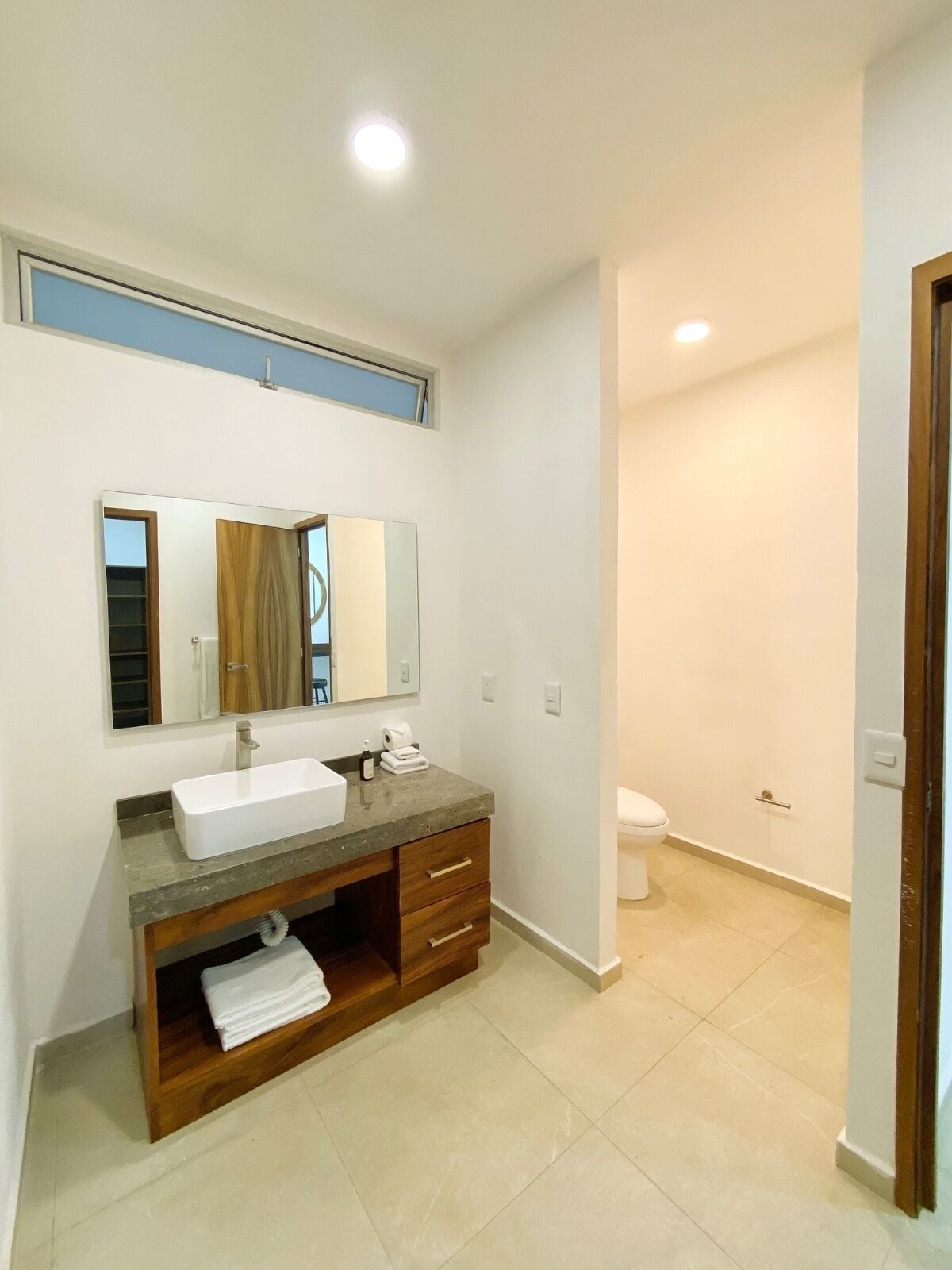 Une salle de bain moderne avec un lavabo blanc, un meuble-lavabo en bois et un grand miroir.