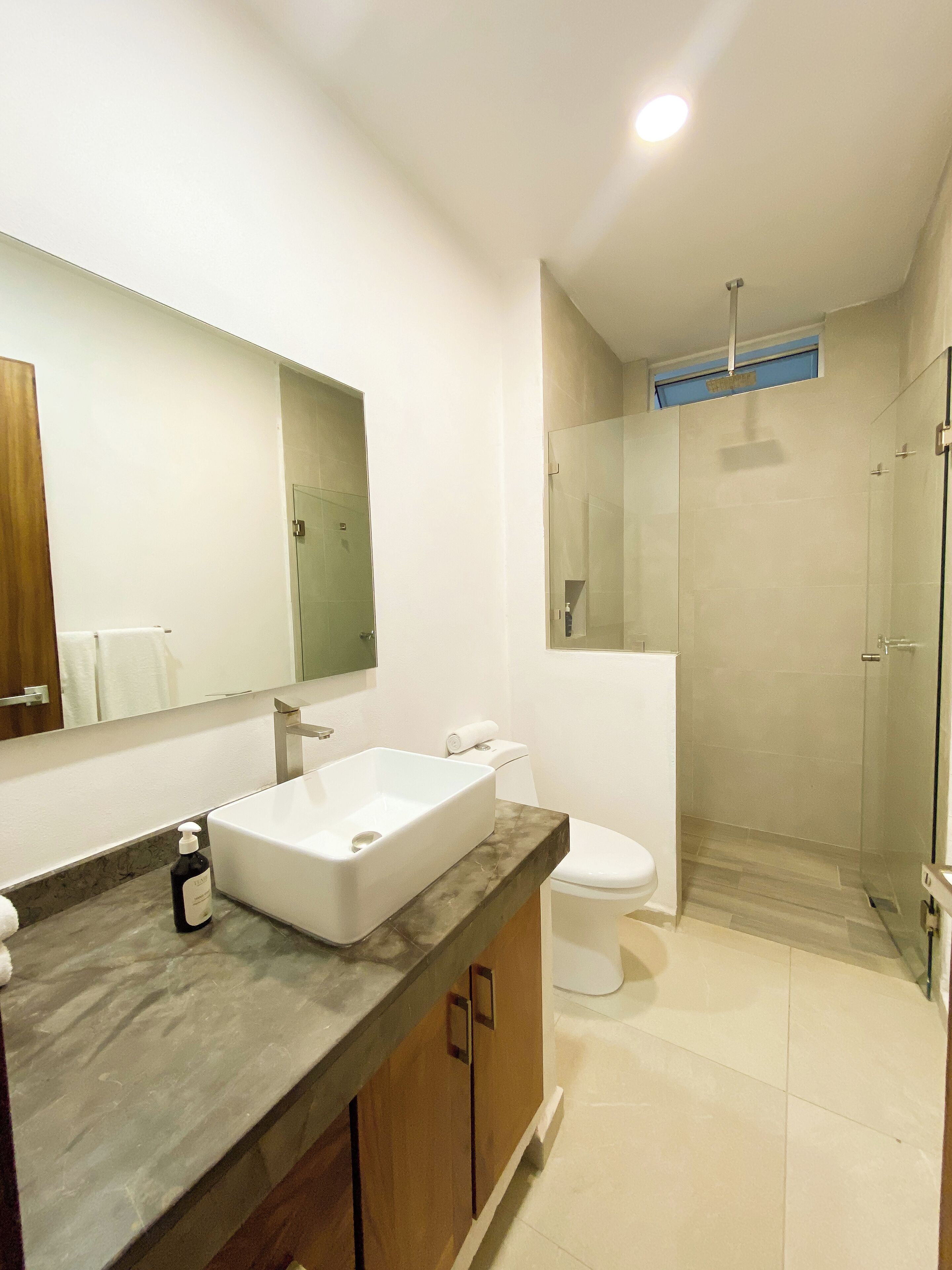 Une salle de bain moderne avec un grand miroir, un lavabo rectangulaire, des toilettes et une douche à parois de verre.