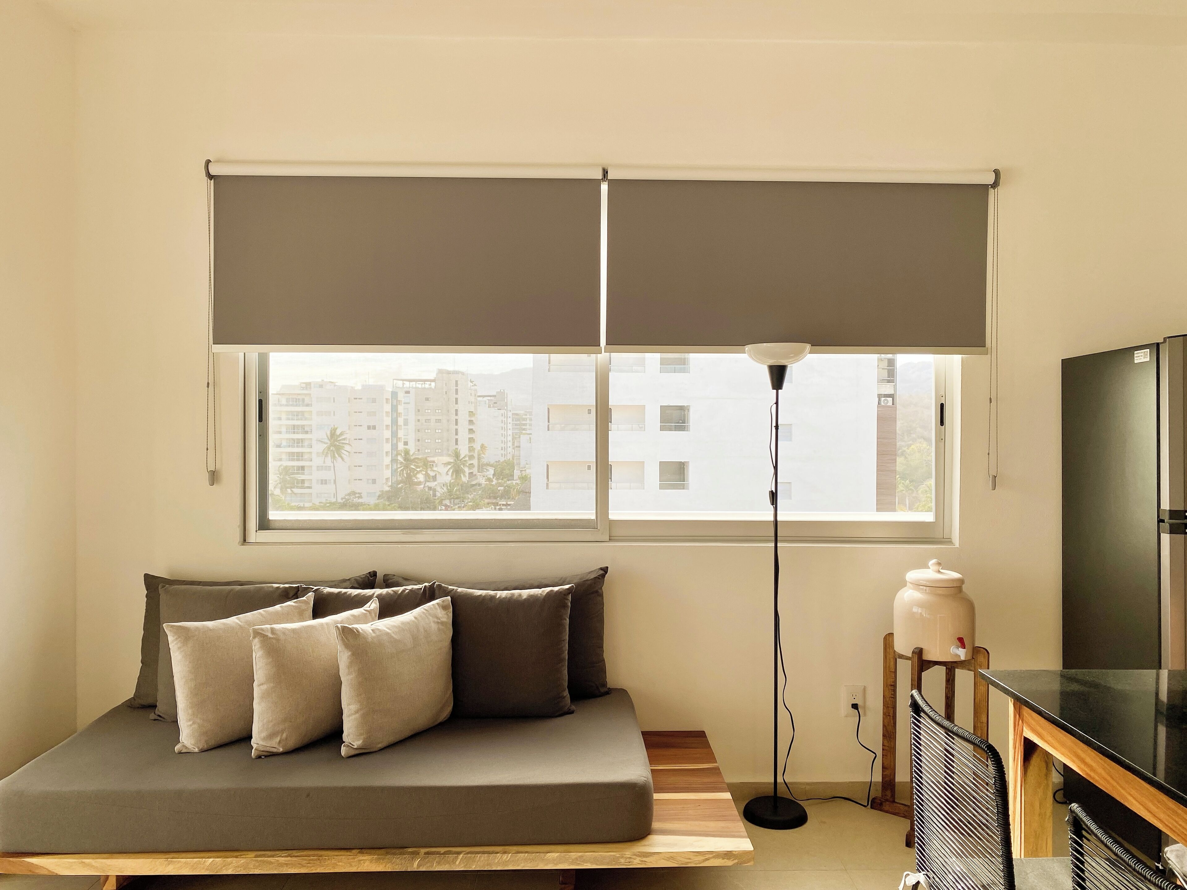 Una sala de estar moderna con un sofá, una lámpara de pie, un televisor y una ventana con vistas a edificios.