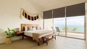 Ein Schlafzimmer mit einem großen Bett, einer Bank, einem Nachttisch, einer Topfpflanze und Meerblick durch eine Schiebetür.