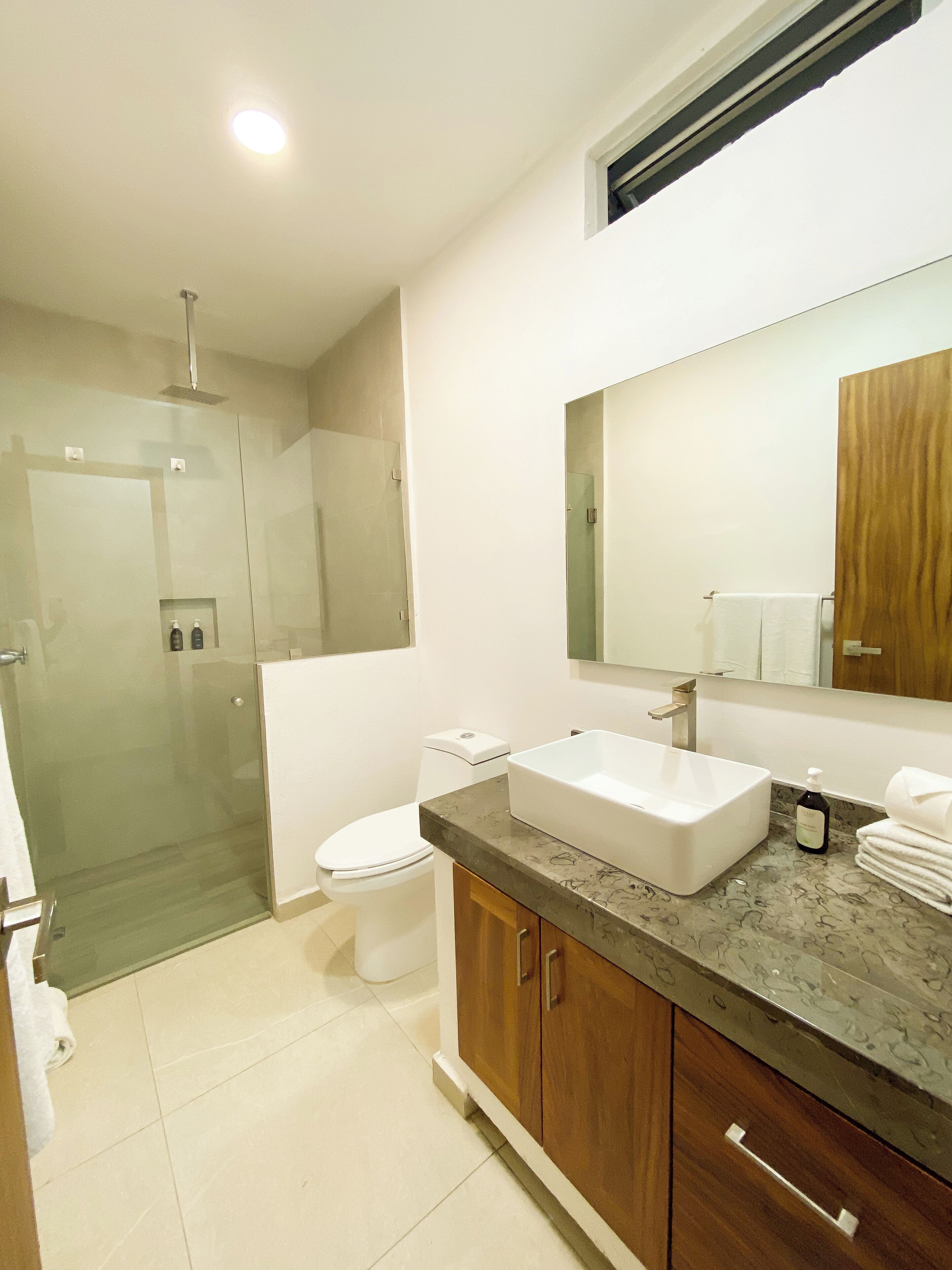 A modern bathroom with a glass shower enclosure, a white toilet, a large sink, and wooden cabinets.