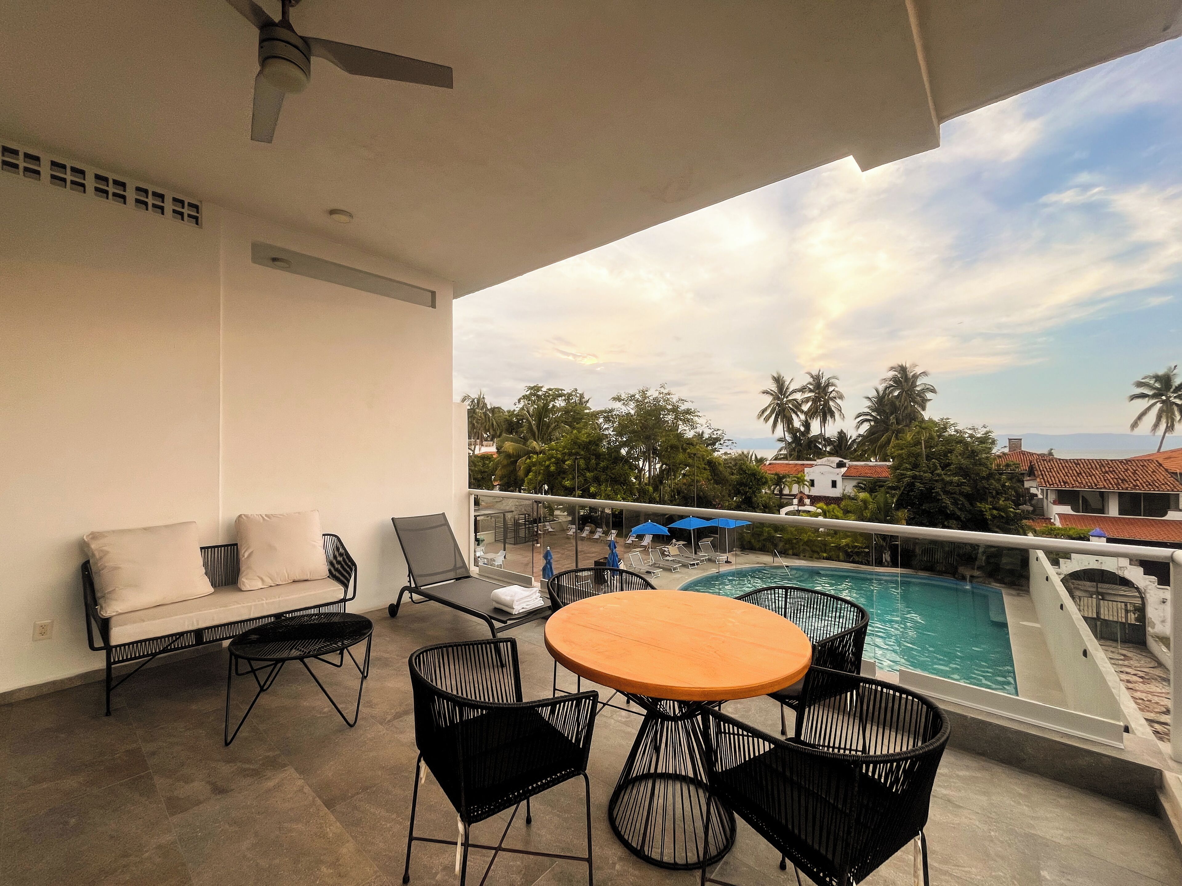 A balcony with a pool, lounge chairs, and a table.