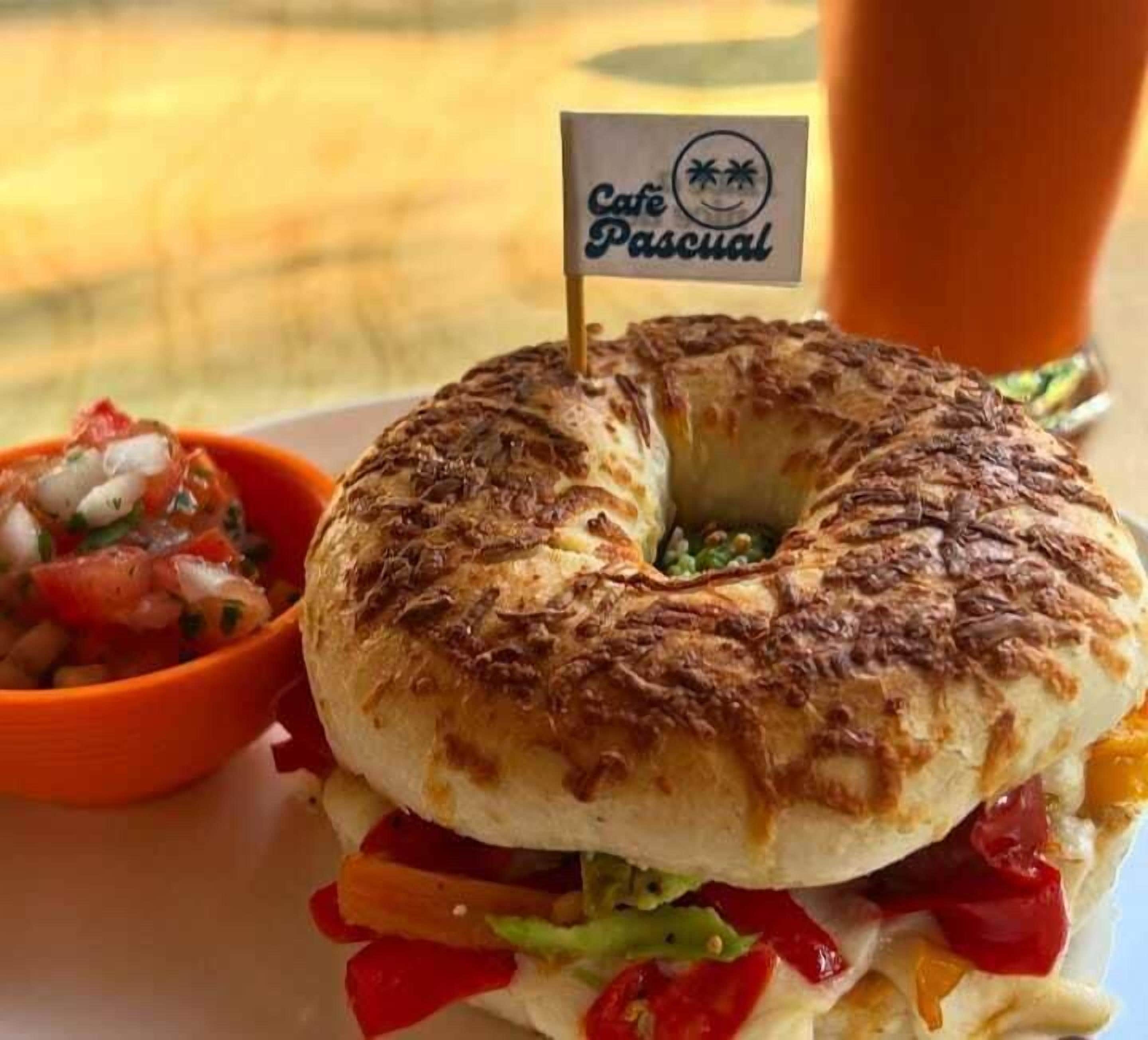 Un sándwich de desayuno con una bandera encima, una guarnición de salsa y una bebida al fondo.