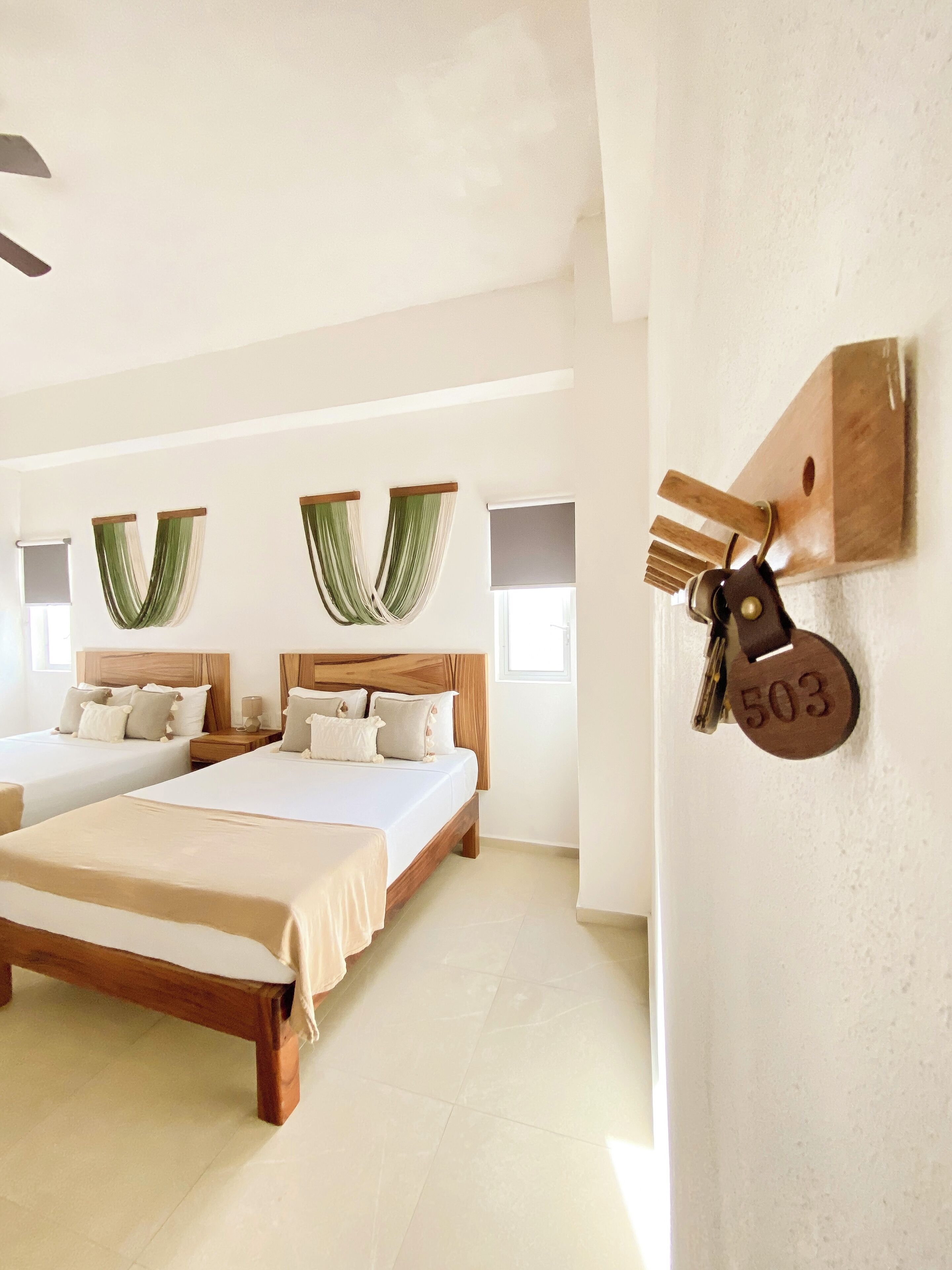 A hotel room with two beds, a wooden headboard, a wall-mounted key holder, and a large window.