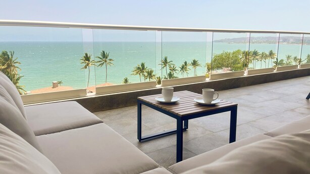 Un balcon avec vue sur la mer, une table en bois avec deux tasses et un canapé.