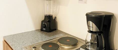 Una kitchenette con cafetera, licuadora y tostadora sobre una encimera de granito.
