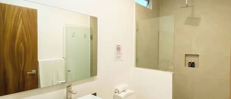 Un baño moderno con un espejo grande, un lavabo, un inodoro y una zona de ducha.