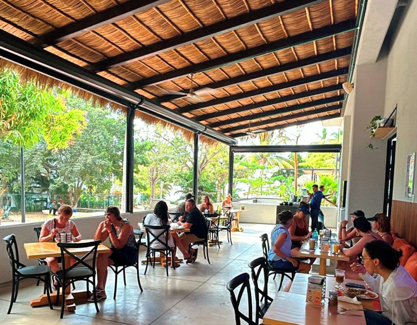 An outdoor café with tables and chairs, surrounded by greenery.