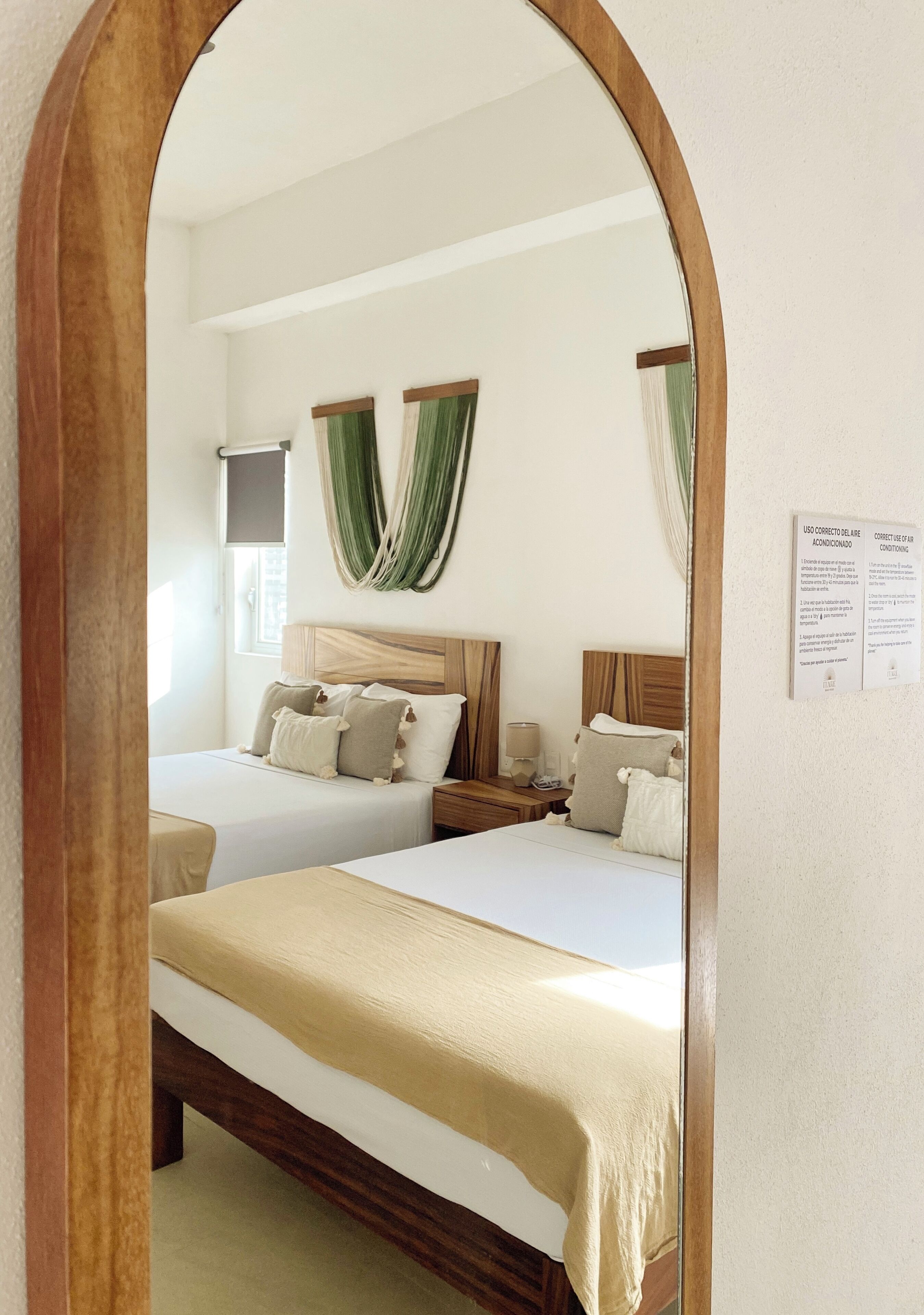 Habitación de hotel con dos camas, cabecero de madera, un espejo y una ventana con cortinas.