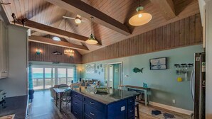 A spacious kitchen with a large island, wooden ceiling beams, and a view to the outside. - Albion: Dive Into Oceanfront Bliss! (Topsail Beach)