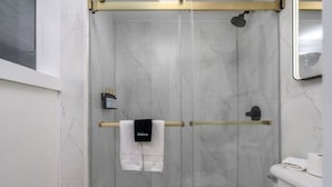 Een moderne badkamer met een douchecabine van glas, een toilet en een handdoekrek met een witte handdoek.