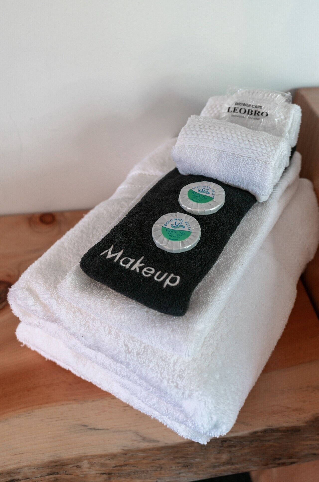 A white towel with a black strip labeled 'Makeup' and two white caps labeled 'BERGMAN KELLY WHITE TEA BATH SOAP' on a wooden surface.