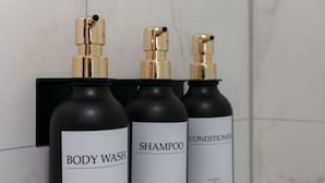 Drie flessen douchegel, shampoo en conditioner bevestigd aan een zwarte muur.